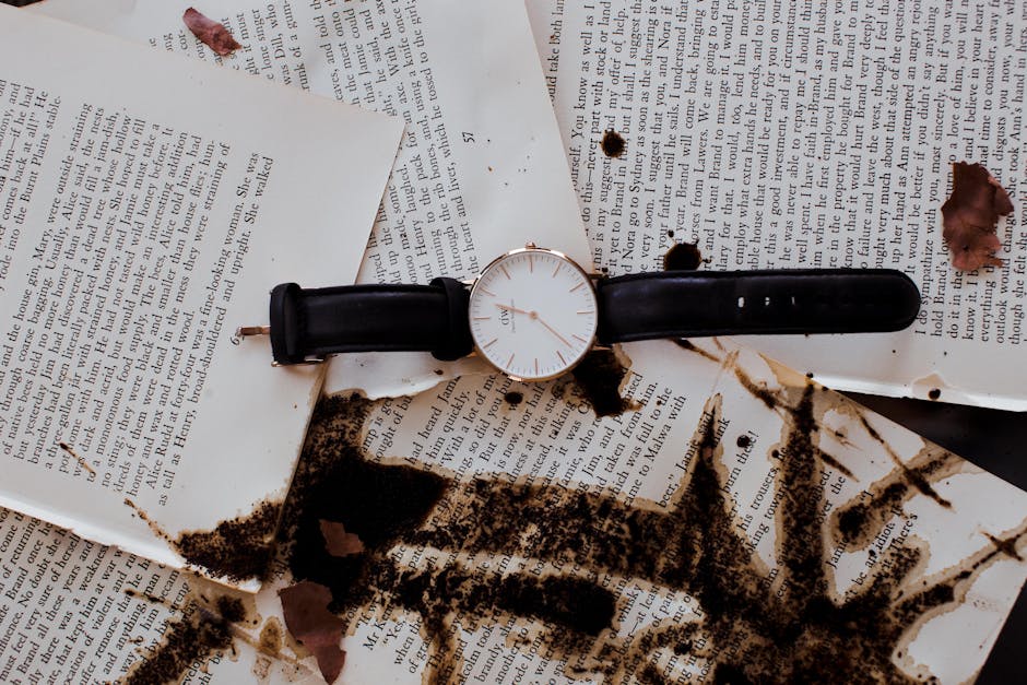 A stylish analog wristwatch on book pages with coffee stains, creating a vintage and artistic feel.