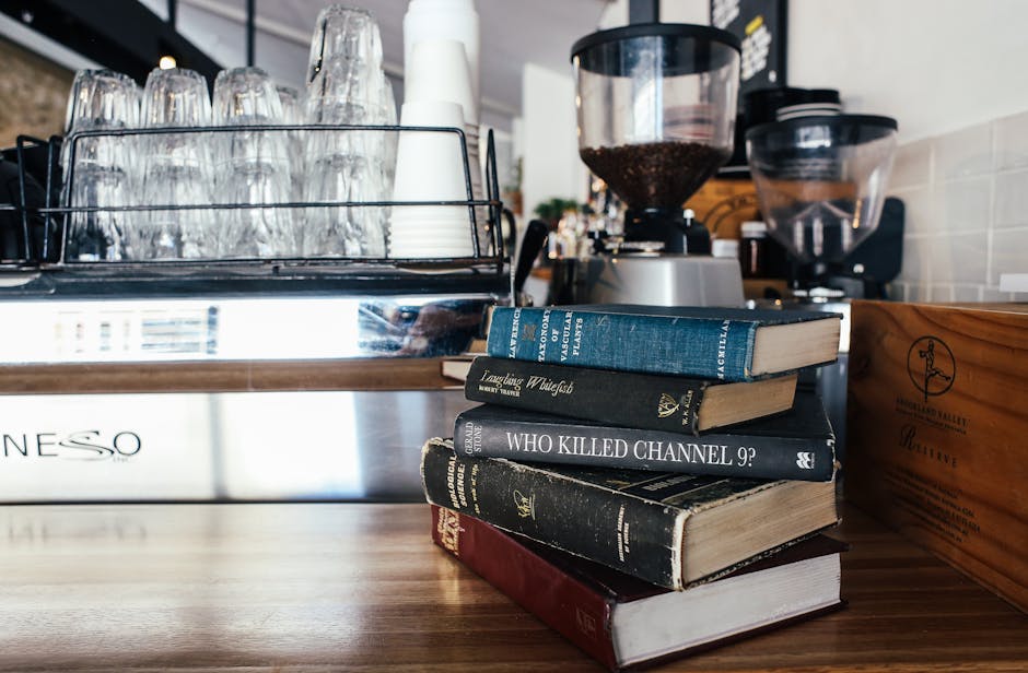 Stack of books beside coffee grinder and glassware in a cozy café setting.